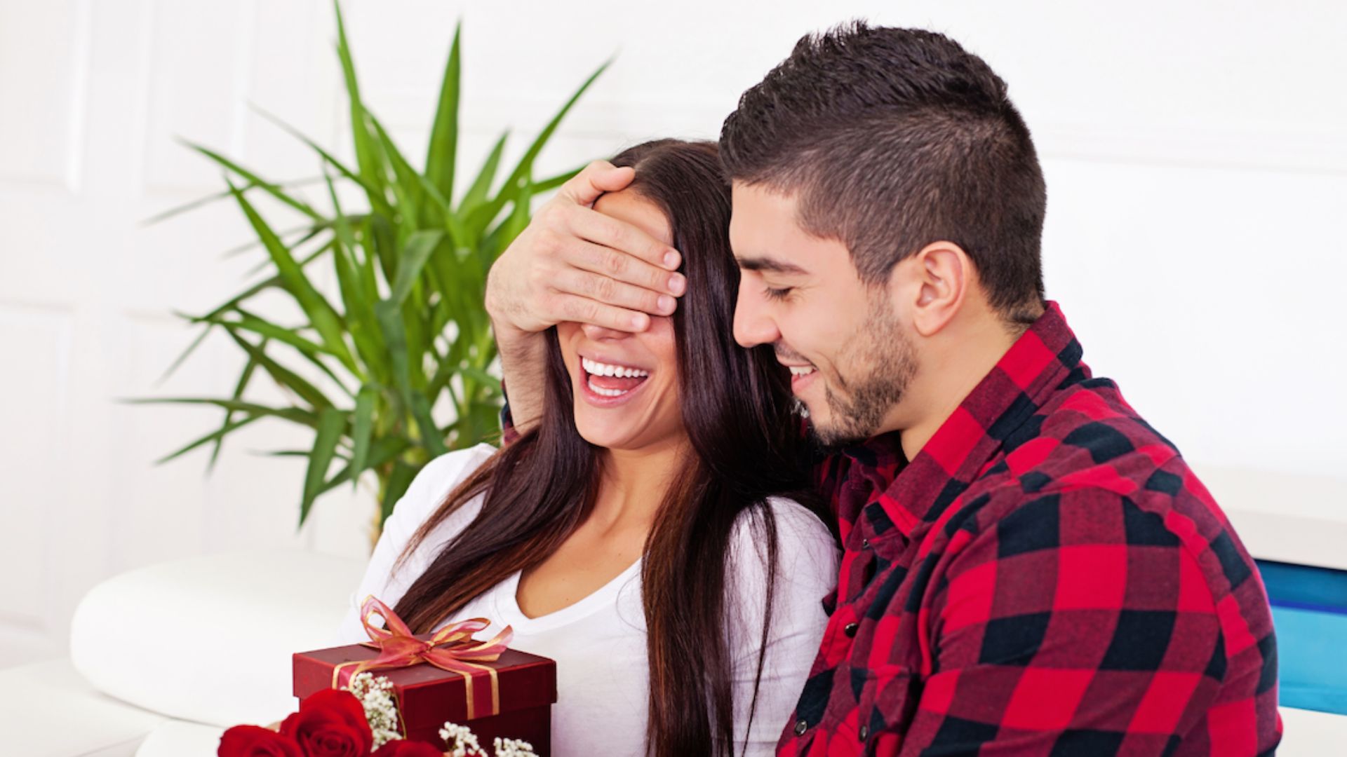 a man closing his wife' eyes while holding a gift